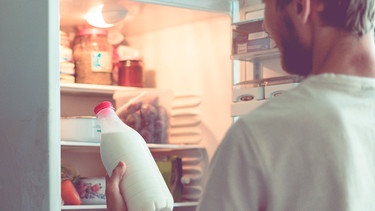 Mann hält Milchflasche vor Kühlschrank | Bild: mauritius images  Mikhail Rudenko  Alamy  Alamy Stock Photos